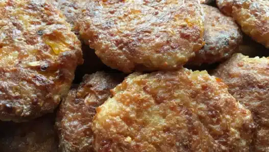 Piatto di polpette di patate e zucchine dorate al forno servite con prezzemolo fresco su un vassoio.
