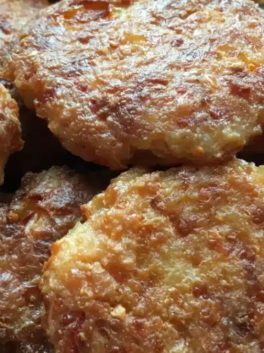 Piatto di polpette di patate e zucchine dorate al forno servite con prezzemolo fresco su un vassoio.