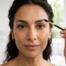 Ritratto ravvicinato di una donna elegante over 40 che definisce l'arcata sopraccigliare, mostrando come una forma curata ringiovanisca e sollevi lo sguardo.