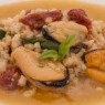 Un piatto di pasta fregola con cozze e pomodori secchi, guarnito con basilico fresco.