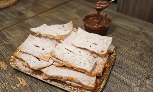 Chiacchiere di Carnevale friabili e piene di bolle spolverate con zucchero a velo su un vassoio