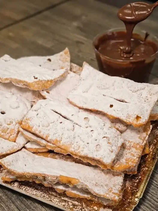 Chiacchiere di Carnevale friabili e piene di bolle spolverate con zucchero a velo su un vassoio