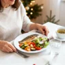 Donna italiana a tavola con dieta leggera prima di Natale: pesce grigliato, verdure e tisana in ambiente natalizio luminoso