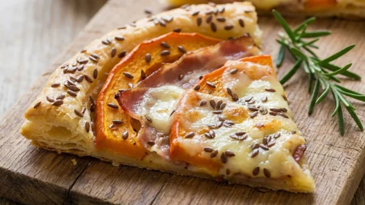 Trancio di sfogliata salata con zucca arancione, fette di speck e taleggio fuso in superficie, cosparso di semi di lino