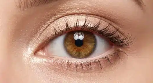 Un primo piano macro di un occhio femminile spalancato e luminoso, che mostra un trucco studiato per ingrandirlo con matita chiara nella rima interna e ombretto scintillante.