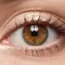Un primo piano macro di un occhio femminile spalancato e luminoso, che mostra un trucco studiato per ingrandirlo con matita chiara nella rima interna e ombretto scintillante.