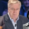 Primo piano di Claudio Lippi sorridente durante una trasmissione televisiva, a contrasto con la notizia del ricovero