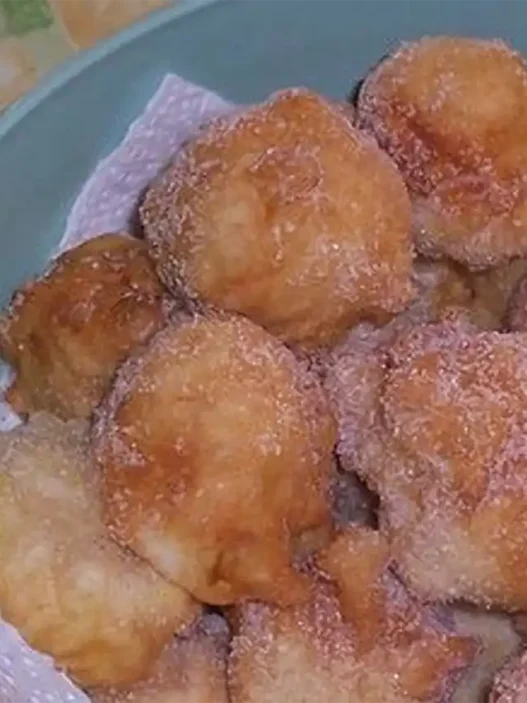 Piatto di frittelle di mele dorate spolverate con zucchero a velo su tavolo di legno