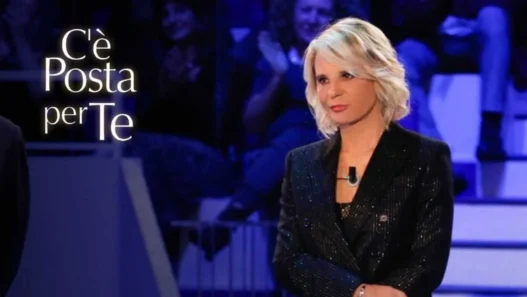 Maria De Filippi sorridente in studio con la busta di C'è Posta per Te