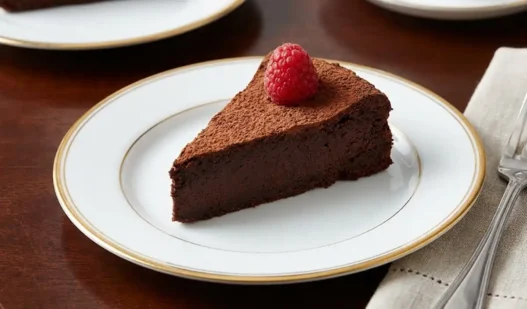 Una fetta di torta al cioccolato densa e cremosa su un piattino elegante, decorata con un lampone fresco.