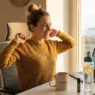 Una donna sorridente si sgranchisce in ufficio durante il pomeriggio, con luce naturale, acqua al limone e tazza PiùDonna sulla scrivania, per contrastare il calo pomeridiano.