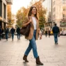 Una donna elegante cammina in città indossando un blazer leggero color cammello e stivaletti estivi, perfetto look di transizione per settembre.