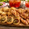 Un tagliere di legno rustico ricco di antipasti di pasta sfoglia appena sfornati, come girelle e grissini, perfetti per il pranzo di Ferragosto.