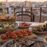 avola apparecchiata al tramonto con piatti freschi a base di fichi, pomodori e melanzane per una perfetta cena estiva in città.