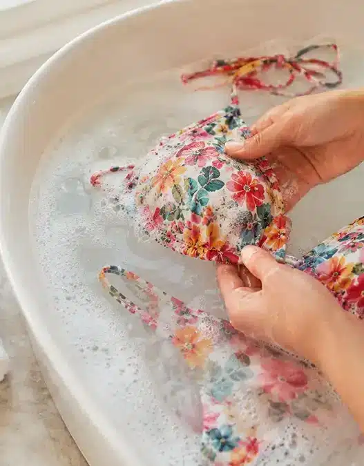 Un costume da bagno colorato in ammollo in una bacinella d'acqua fredda con sapone delicato, il metodo migliore per lavare i costumi ed eliminare la salsedine.