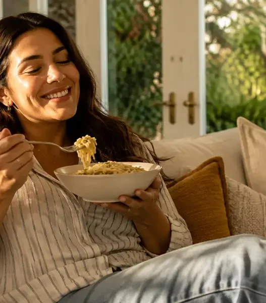 Una donna sorridente e rilassata si gode il suo comfort food a fine agosto, combattendo lo stress da rientro senza sensi di colpa