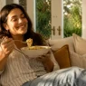 Una donna sorridente e rilassata si gode il suo comfort food a fine agosto, combattendo lo stress da rientro senza sensi di colpa
