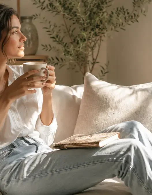 Donna che si rilassa sul divano con una tazza di tè, riflettendo sugli obiettivi autunnali per sconfiggere l'ansia da rientro.