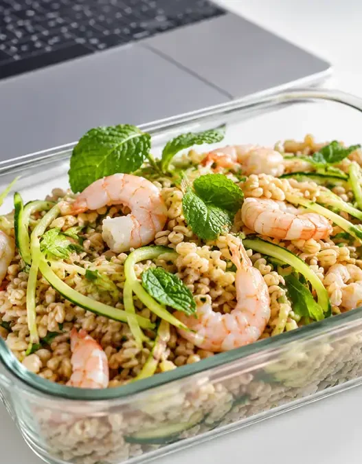 Schiscetta estiva in vetro con insalata di farro, gamberetti e zucchine crude tagliate a julienne, ideale per il pranzo in ufficio