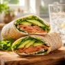 Un appetitoso wrap integrale tagliato a metà, ripieno di fette di salmone affumicato, morbido avocado e rucola fresca, servito su un tagliere di legno rustico.