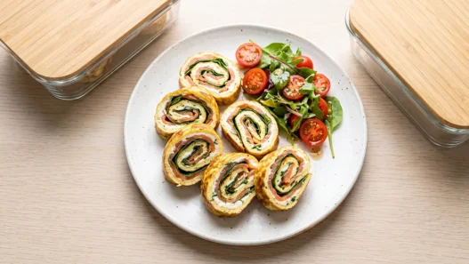 Girelle di frittata sottile farcite con salmone affumicato e formaggio spalmabile, disposte su un piatto bianco.
