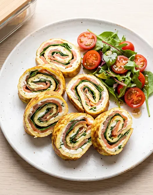 Girelle di frittata sottile farcite con salmone affumicato e formaggio spalmabile, disposte su un piatto bianco.