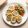Girelle di frittata sottile farcite con salmone affumicato e formaggio spalmabile, disposte su un piatto bianco.
