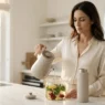 Donna elegante prepara una tisana naturale in una cucina luminosa. Sul piano in marmo una borraccia termica, simbolo di idratazione e lifestyle intelligente.