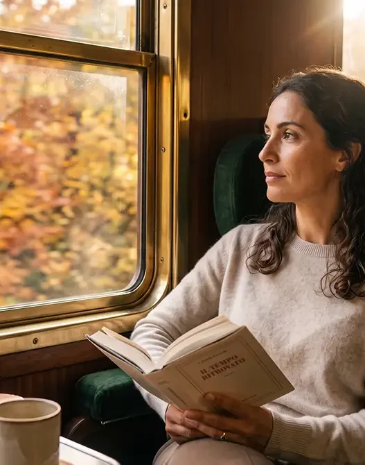 Donna sofisticata in viaggio da sola in treno mentre legge un libro guardando i colori caldi dell'autunno dal finestrino