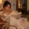 Donna rilassata legge un libro sul divano con una tazza calda, simbolo di digital detox e benessere serale.